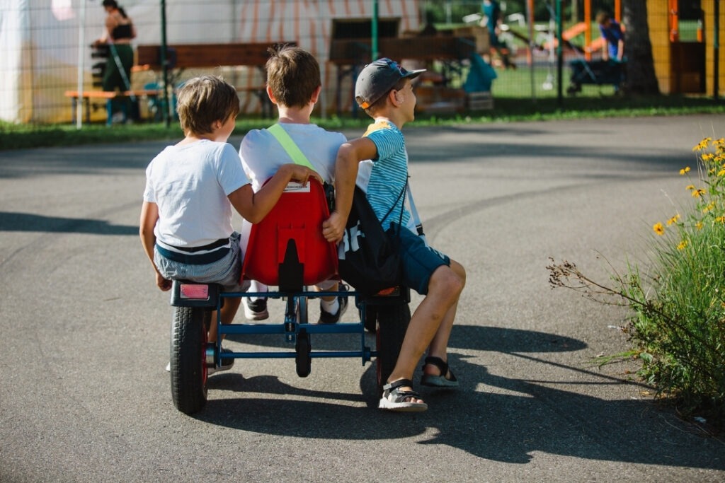 Spielkinder fahren gemeinsam mit einem kleinen Fahrzeug über das Gelände der Spielstadt Bad Kresselnau.