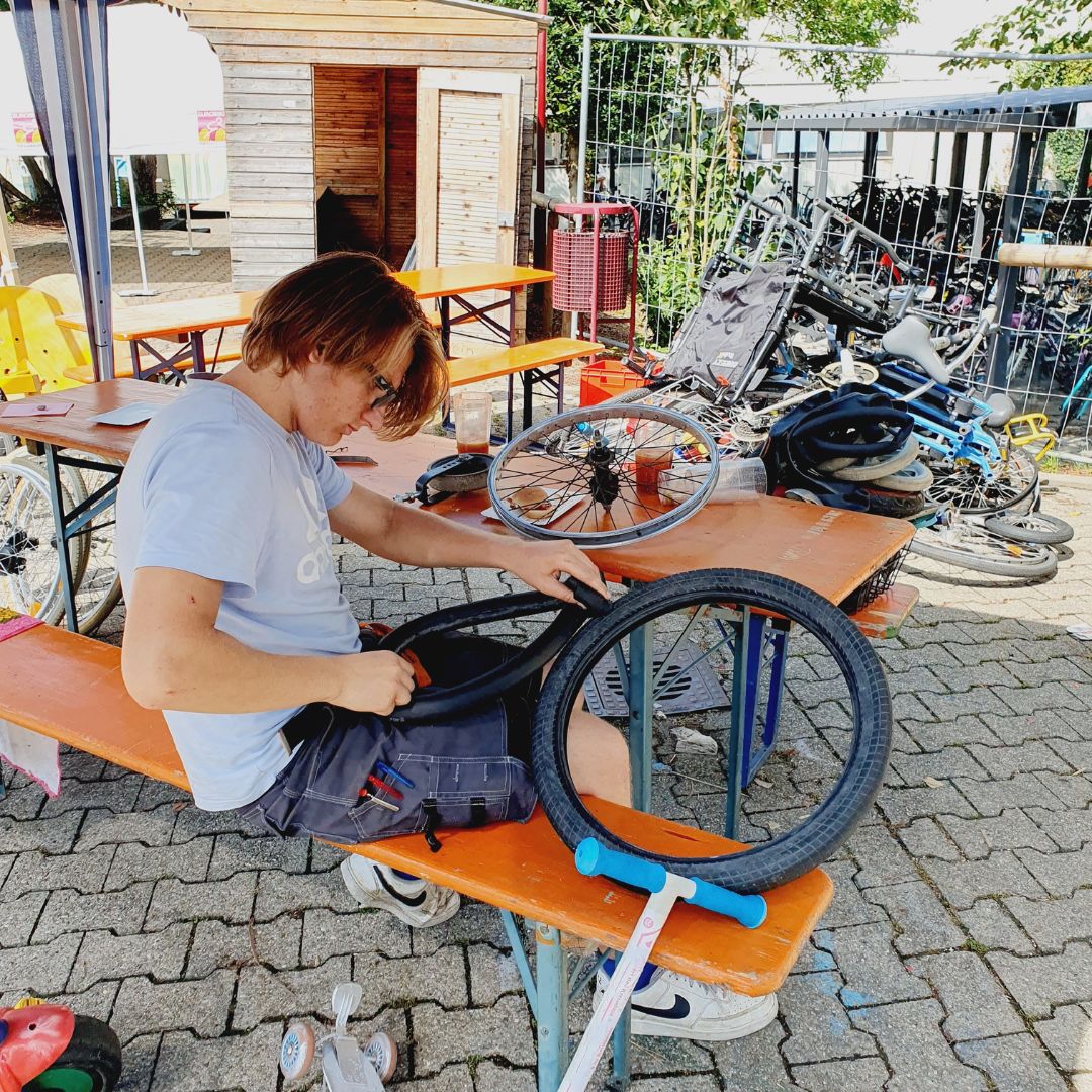 Ein jugendlicher Helfer repariert ein Fahrrad in der Arbeitsstelle Fahrradwerkstatt der Spielstadt Bad Kresselnau.