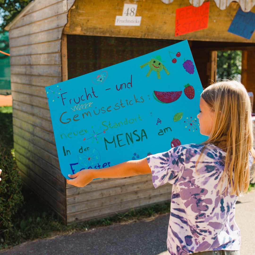 Ein Spielkind präsentiert ein gestaltetes Plakat in der Arbeitsstelle Werbeagentur der Spielstadt Bad Kresselnau.