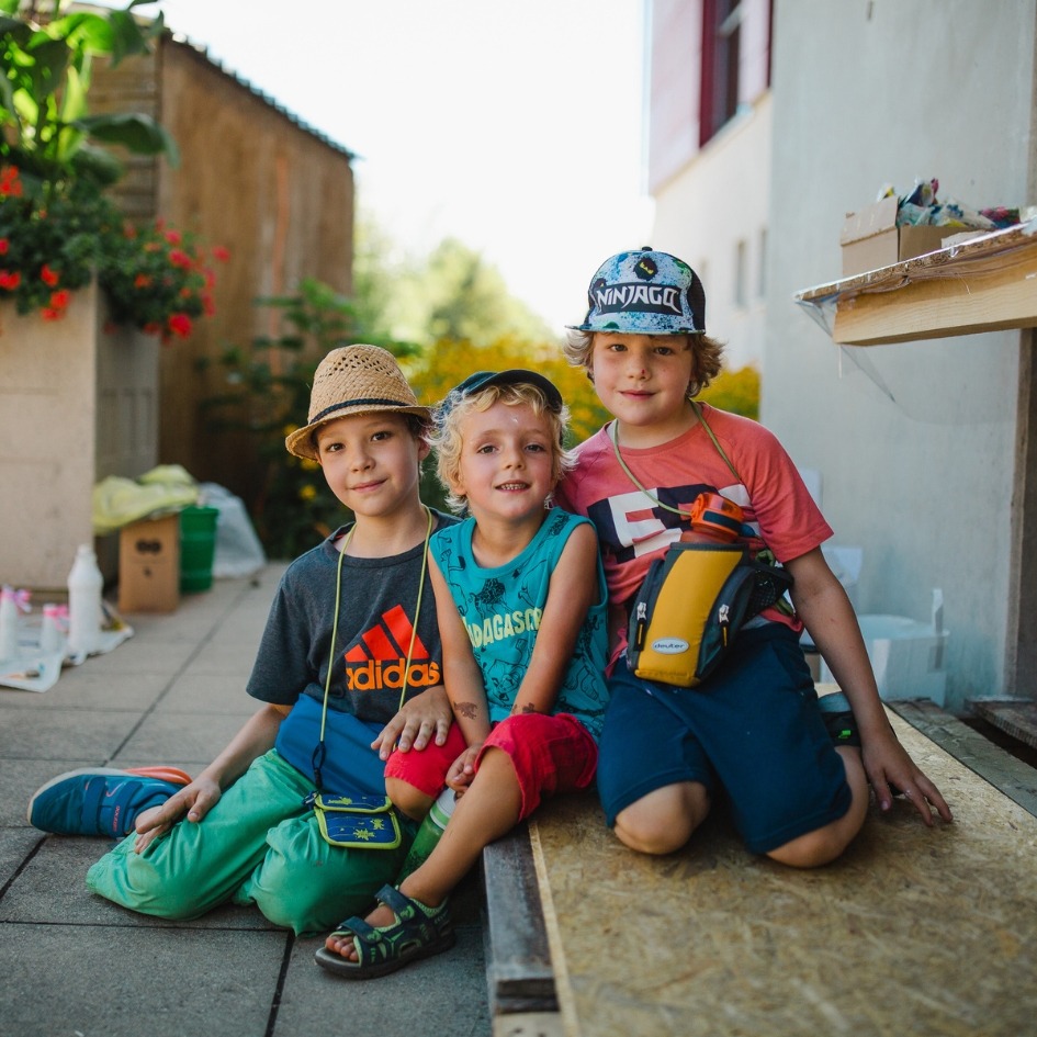 Drei Spielkinder der Spielstadt Bad Kresselnau sitzen gemeinsam und schauen in die Kamera.
